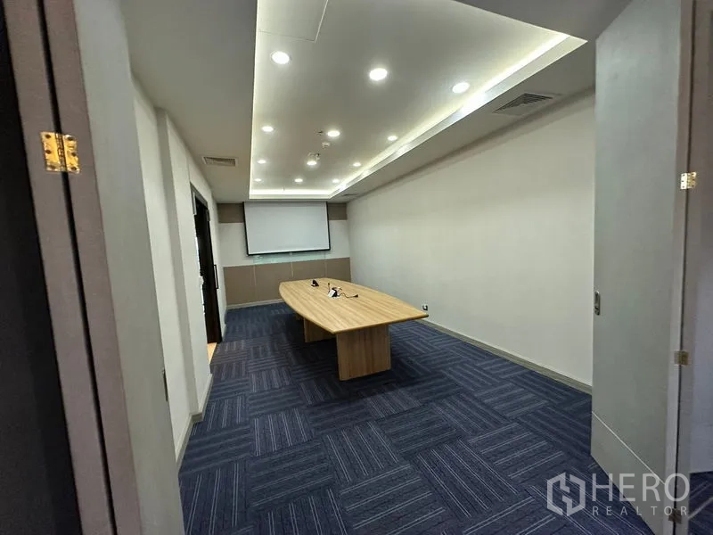 Office Space for rent - Boardroom with long table, projector screen and LED ceiling lights over blue carpet.