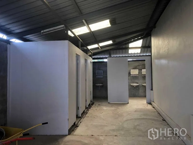 Warehouse for rent in Prawet, Bangkok - Staff washrooms with multiple toilet stalls and sinks under a metal roof.