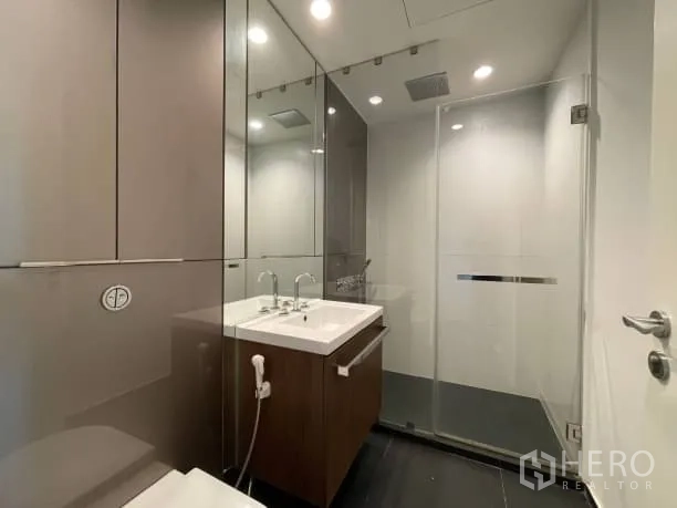 Condominium for rent or sale in Pathum Wan, Bangkok - Modern bathroom with glass-enclosed shower, sleek vanity, mirrored cabinets and recessed lighting.