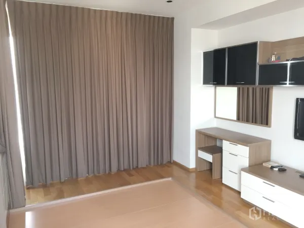 Condominium for rent in Khlong Toei, Bangkok - Second bedroom with hardwood floors, built-in cabinets, work desk, and floor-to-ceiling curtains.