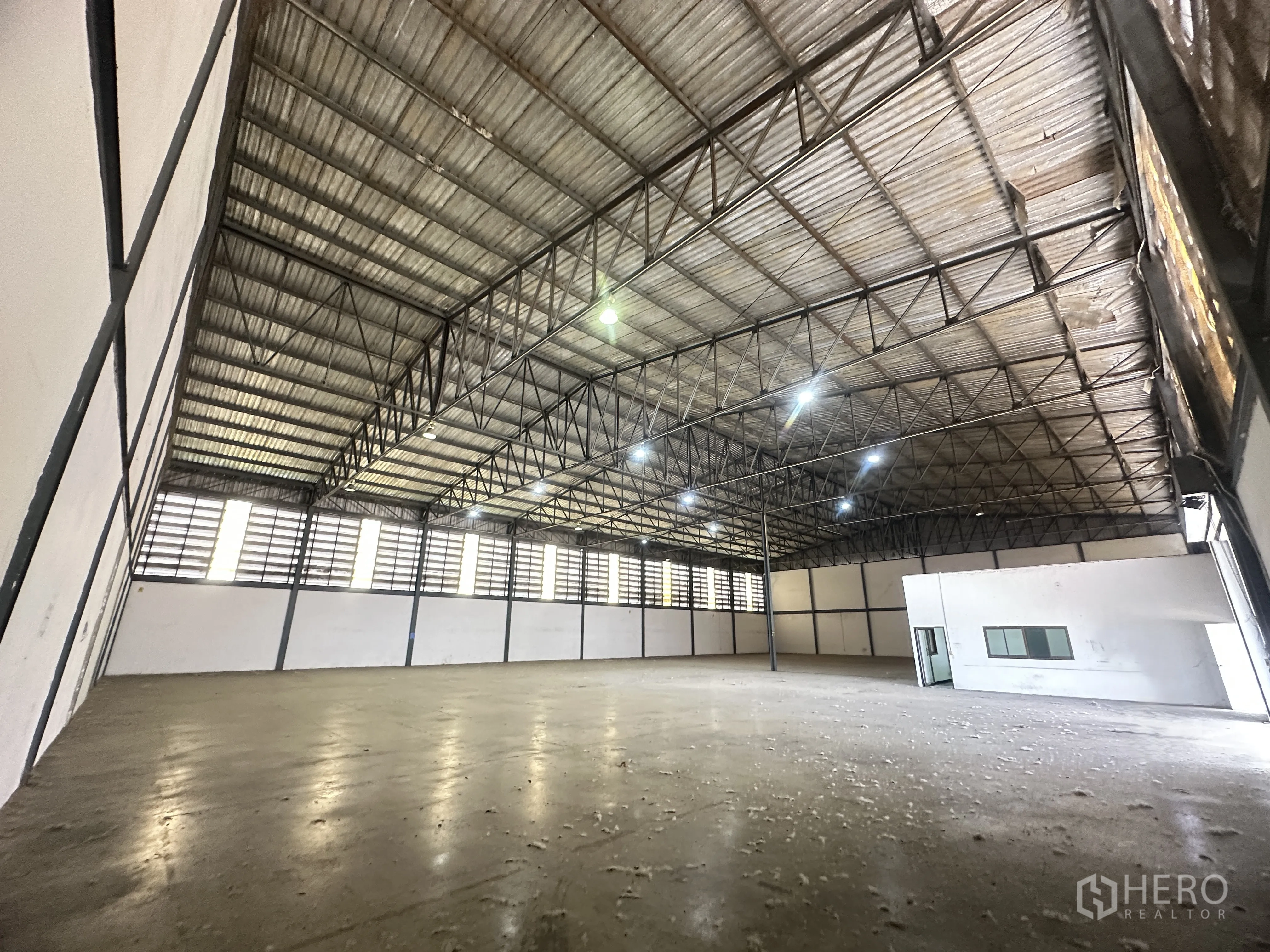 Warehouse for rent in Khlong Luang, Pathum Thani - Wide warehouse interior with steel truss roof, ventilated side panels, and a built-in office block.
