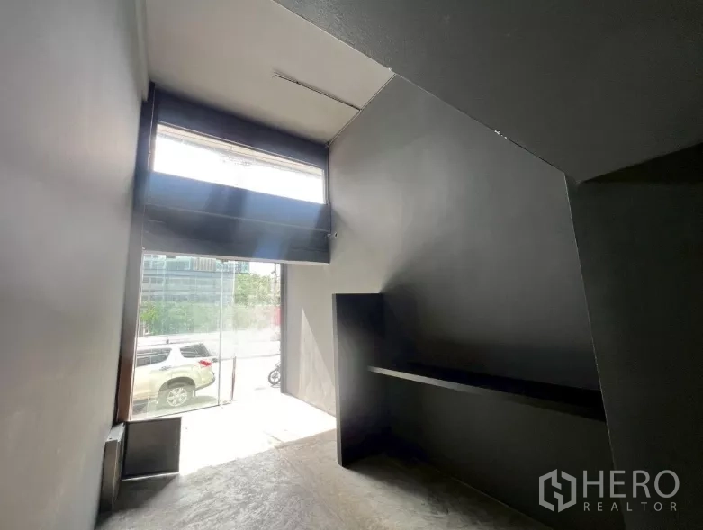 Shophouse for rent in Watthana, Bangkok - Street-facing retail area with a tall glass entry and dark-painted walls.