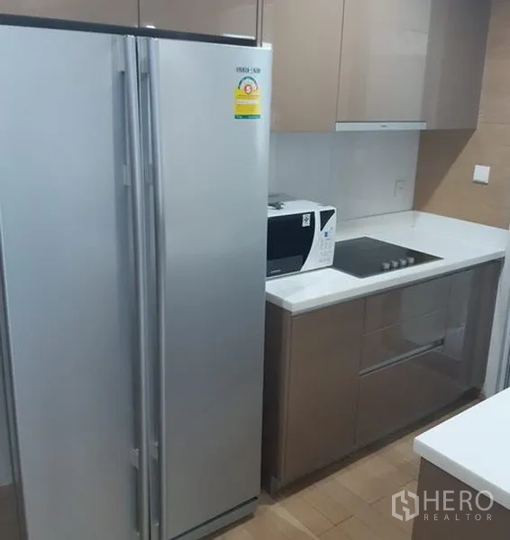 Condominium for rent in Khlong Toei, Bangkok - Modern condo kitchen with side-by-side fridge, microwave and built-in electric cooktop.