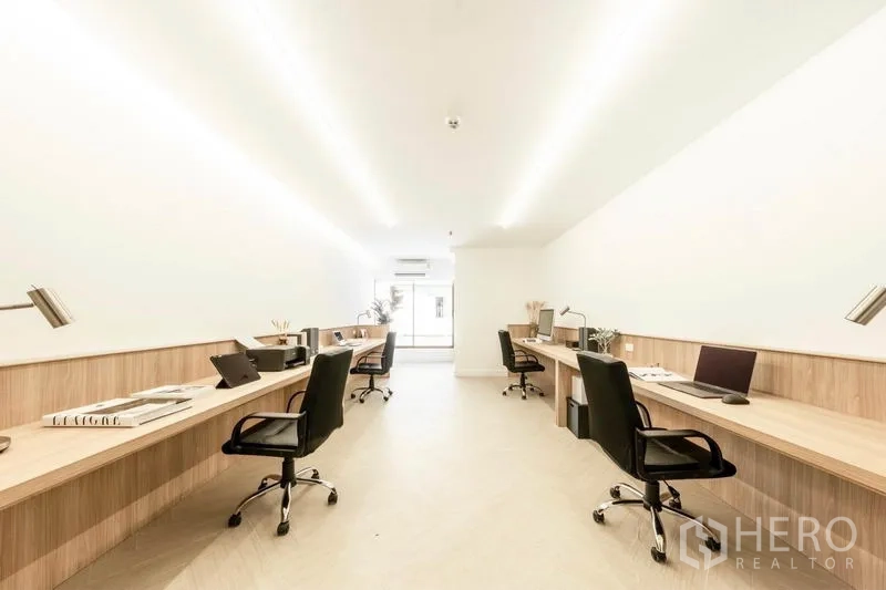 Office Space for rent in Khlong Toei, Bangkok - Bright open-plan office with long built-in wooden desks, task lamps and ergonomic chairs leading to a window, Phra Khanong.