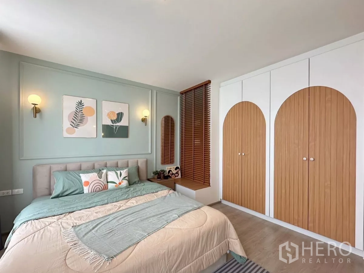 Townhouse for rent in Prawet, Bangkok - Master bedroom with pastel bedding, wall sconces and arched wood-paneled wardrobes.