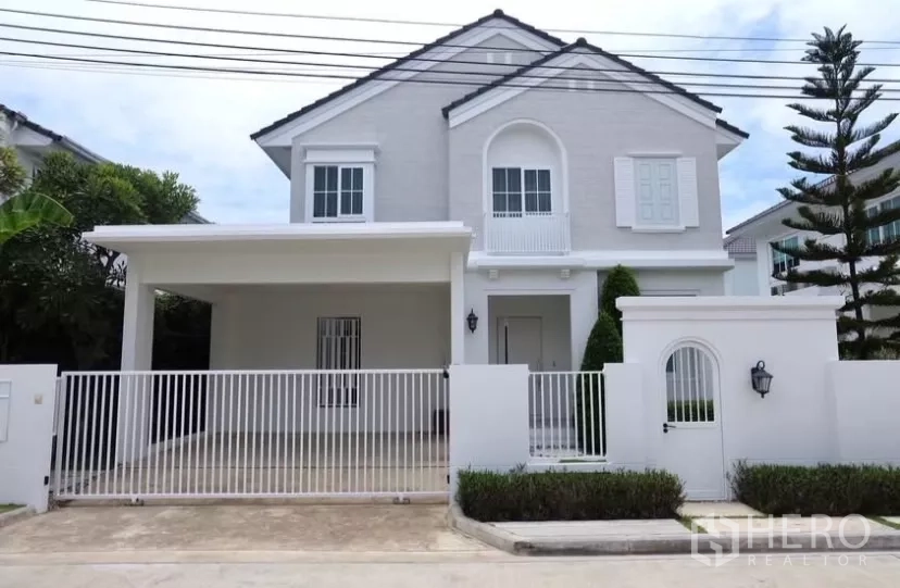 Detached House for rent in Bang Phli, Samut Prakan - Two-storey white detached house with gated front yard and covered carport in a quiet estate.