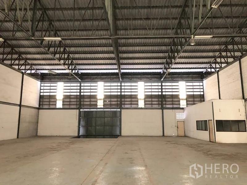 Warehouse for rent in Khlong Luang, Pathum Thani - Large warehouse hall with high steel truss ceiling, louvered clerestory windows and wide metal door.
