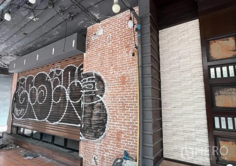 Retail Space for rent in Khlong Toei, Bangkok - Exposed brick exterior wall with roller shutter and string lights, ideal for signage.