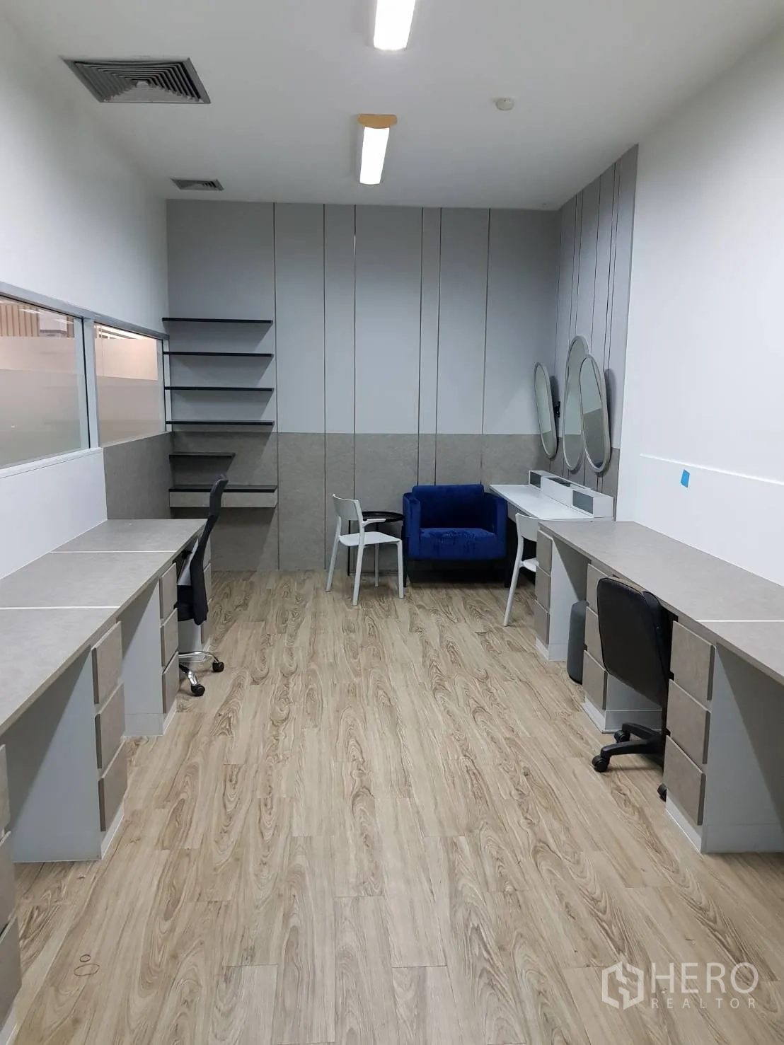 Office Space for rent in Khlong Toei, Bangkok - Workroom with twin rows of built-in desks, shelving, round mirrors, and a blue sofa under ceiling lights.