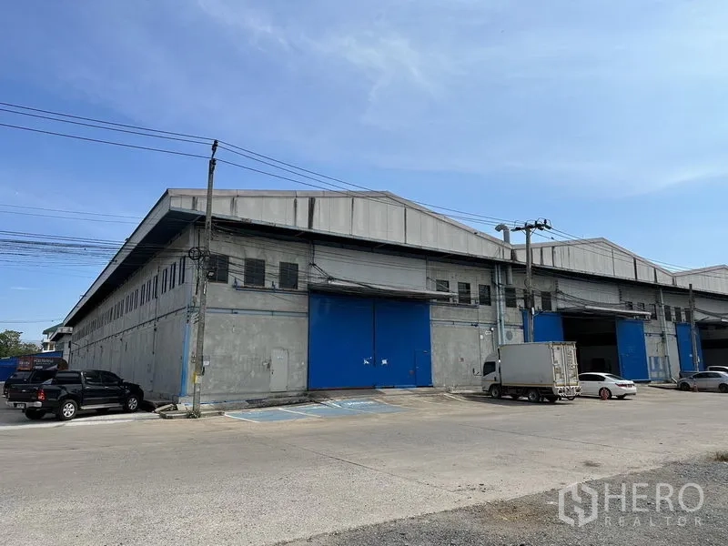 Warehouse for rent in Bang Phli, Samut Prakan - Close exterior view of the warehouse facade with a wide blue roller door and truck access bays.