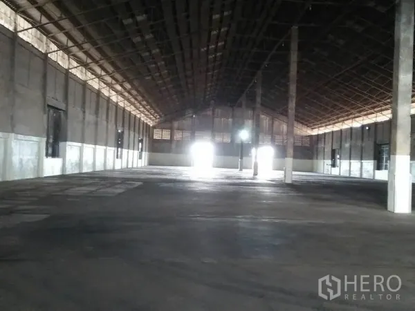 Warehouse for rent in Pathum Thani - Spacious warehouse interior with high steel roof, concrete floor, central columns and bright light at loading doors.