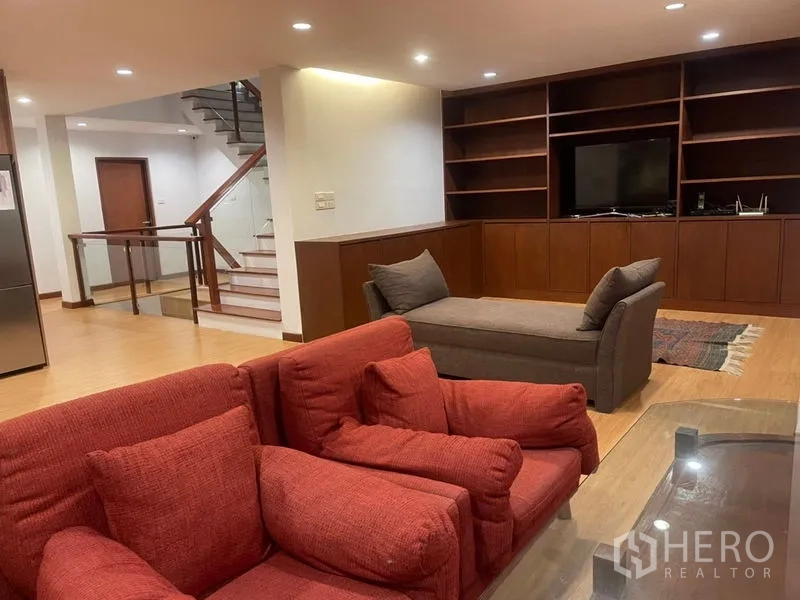 联排别墅 出租在Suan Luang, Bangkok - 宽敞起居室，定制电视柜与书架，木地板和楼梯