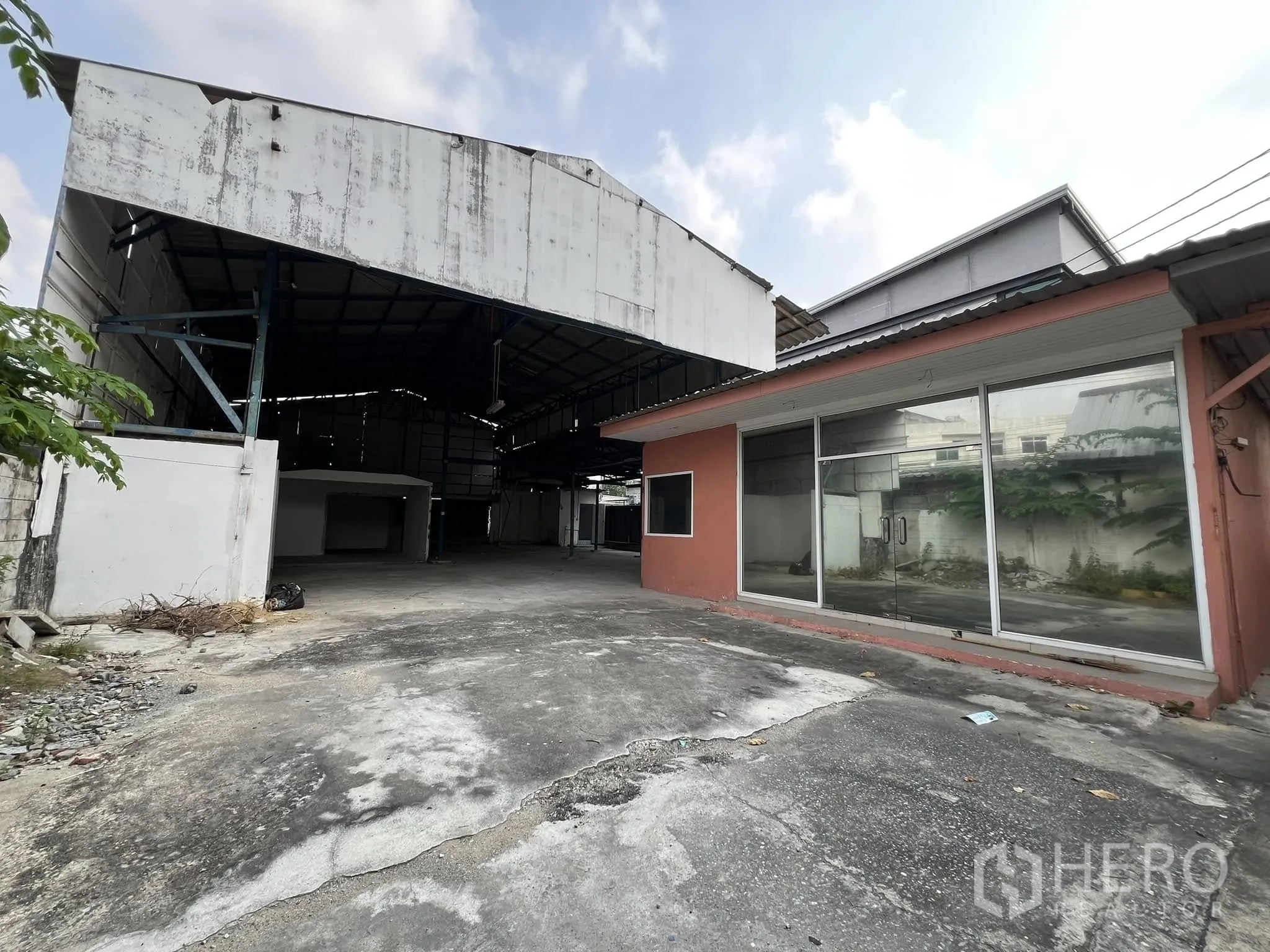Warehouse for rent in Lat Phrao, Bangkok - Front view of an open-sided warehouse with steel roof and a glass-front office beside a concrete yard.