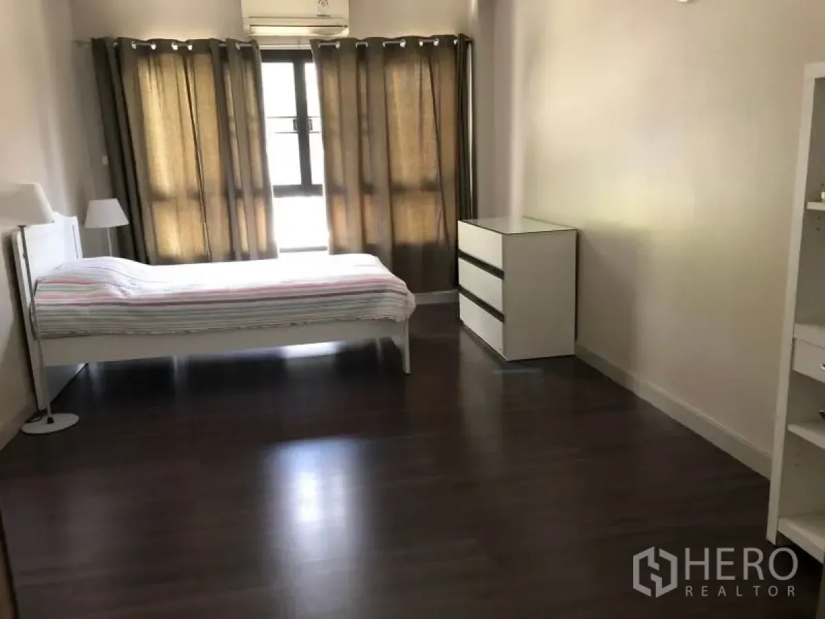 Apartment for rent in Khlong Toei, Bangkok - Spacious bedroom with dark wood floors, large curtained windows, white bedframe and dresser.