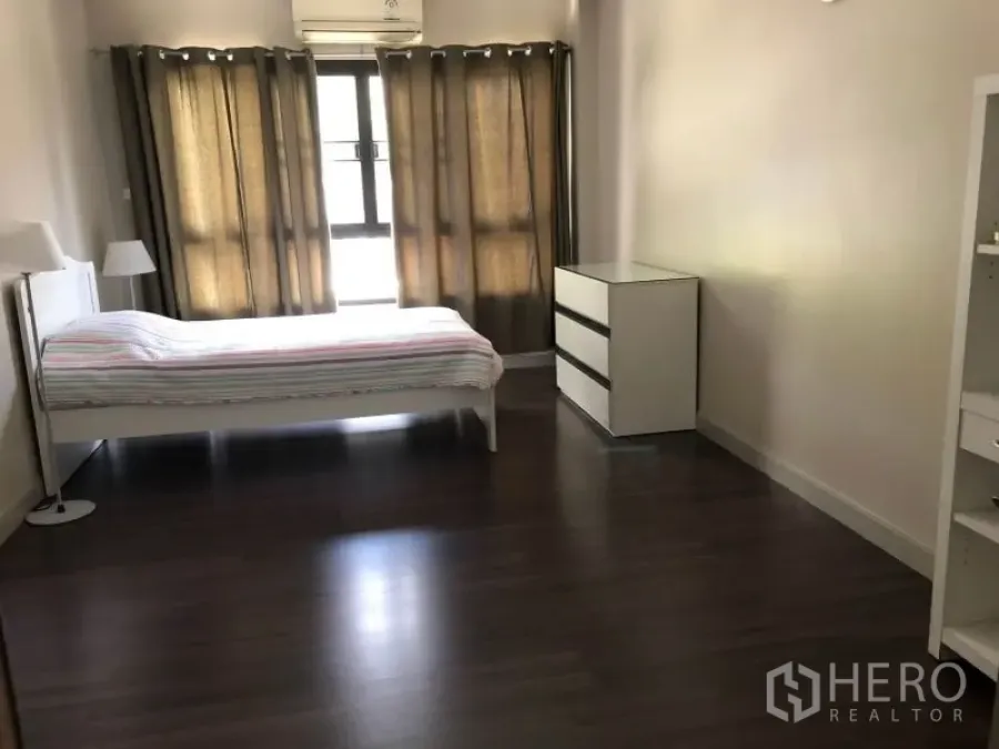 Apartment for rent in Khlong Toei, Bangkok - Spacious bedroom with dark wood floors, large curtained windows, white bedframe and dresser.