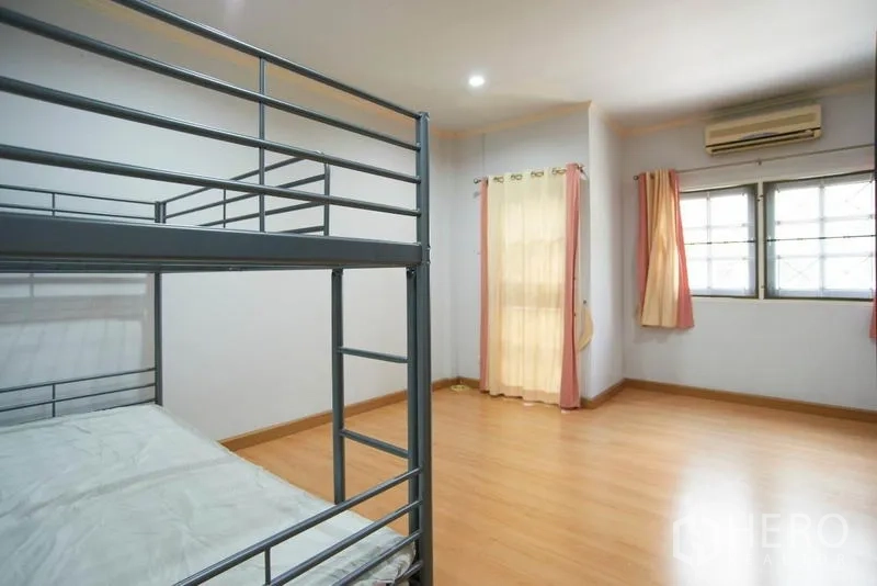 Home Office for rent in Wang Thonglang, Bangkok - Spacious bedroom with wood flooring, air conditioner and a metal bunk bed with curtains.
