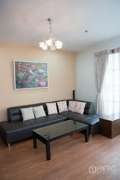 Condominium for rent in Khlong Toei, Bangkok - Cozy lounge corner with black sectional sofa, glass coffee table and chandelier against wood flooring.