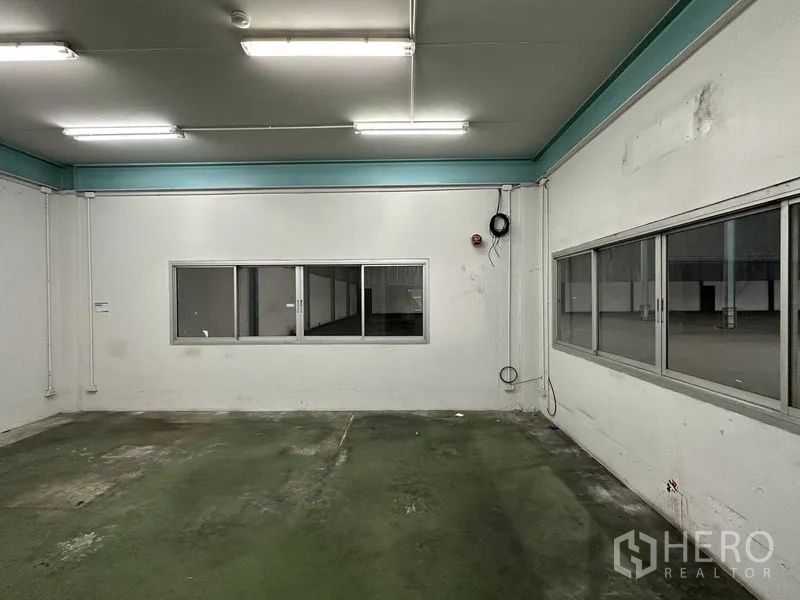 Warehouse for rent in Mueang Samut Prakan, Samut Prakan - Ground-floor office room with windows overlooking the warehouse floor and fluorescent lighting.