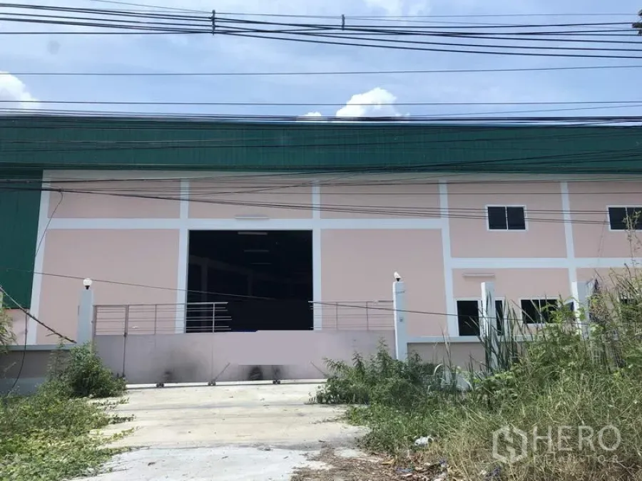 Factory for rent in Pathum Thani - Front exterior of a pink-and-green factory in Lat Lum Kaeo with a wide loading entrance, gated driveway, and roadside power lines.