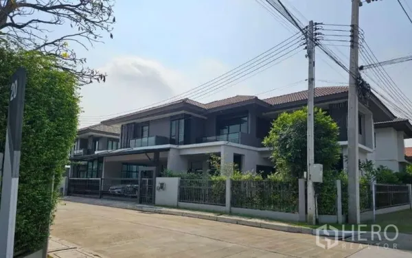 Detached House for sale in Lam Luk Ka, Pathum Thani - Wide street view of the residence with balconies, greenery and tiled roof.