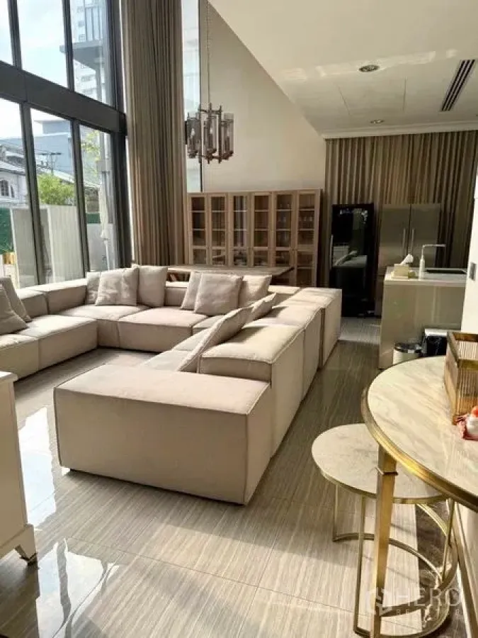 Townhouse for rent in Watthana, Bangkok - Another angle of the double-height living room with sectional and tall windows.