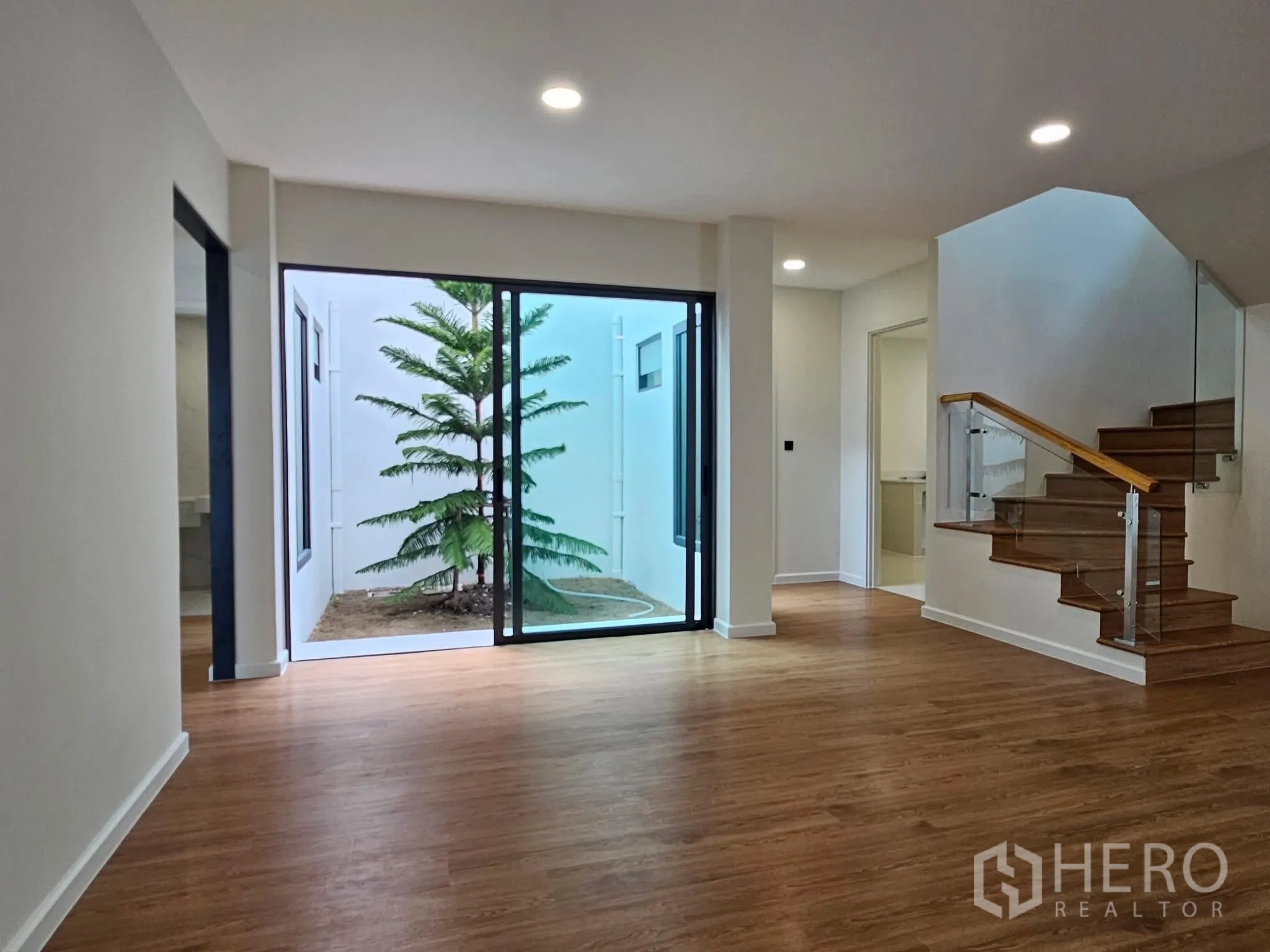 Detached House for sale in Lat Phrao, Bangkok - Living area opening through large sliding glass doors to a private courtyard with a tree.