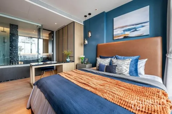Condominium for rent in Khlong Toei, Bangkok - Blue-accent bedroom with glass-walled bathroom, desk and pendant lights