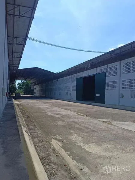 Warehouse for rent in Mueang Rayong, Rayong - Exterior loading lane with a long warehouse facade and large green sliding doors.