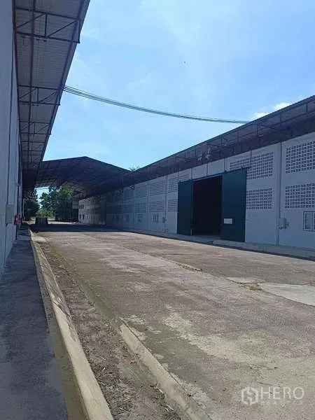 Warehouse for rent in Mueang Rayong, Rayong - Exterior loading lane with a long warehouse facade and large green sliding doors.