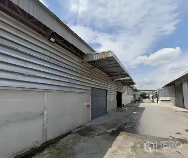 货栈 出租 - 一排金属外墙仓库，带覆盖式装卸区与宽阔卡车通道。