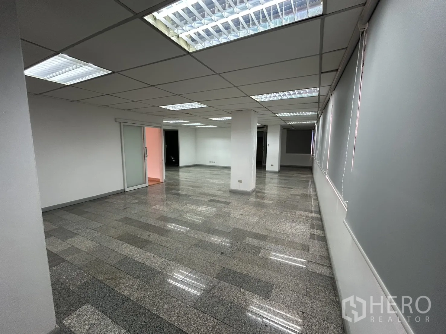 Office Space for rent in Khlong Toei, Bangkok - Open office zone with drop ceiling grid, fluorescent panels, long windows with blinds, and a sliding glass door.