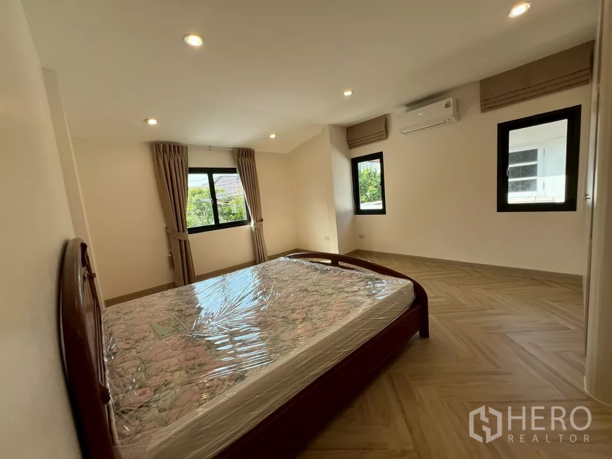 Detached House for rent in Suan Luang, Bangkok - Second bedroom with bed, multiple windows, and warm wood flooring.