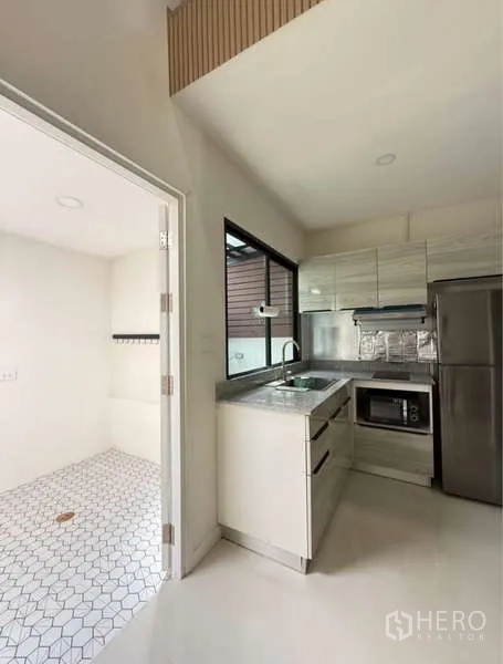 Townhouse for rent in Bang Phli, Samut Prakan - Modern kitchen with white cabinets and stainless appliances beside the laundry area.