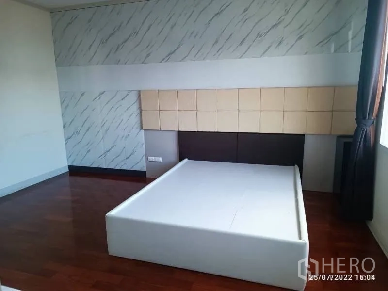 Detached House for sale in Prawet, Bangkok - Spacious bedroom with platform bed frame, wood flooring, accent wall and natural light.