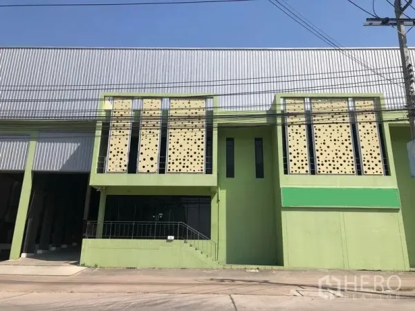 Factory for sale in Bang Phli, Samut Prakan - Factory frontage with perforated facade panels, staircase to glass-front office and adjoining high-bay warehouse under clear blue sky.