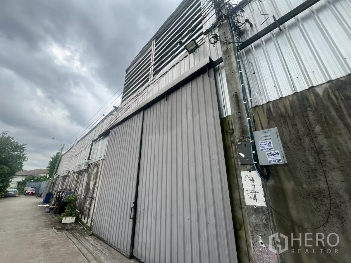 Warehouse for rent - Street-facing corrugated metal warehouse facade with tall sliding gate and utility pole under a cloudy sky.