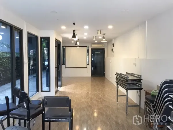 Retail Space for rent in Watthana, Bangkok - Bright open-plan retail interior with wood-look floors, ceiling spotlights and pendants, full-height windows and a wall-mounted projector screen.