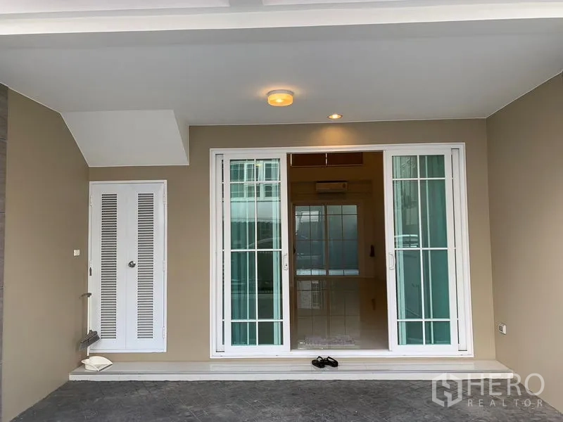 Townhouse for rent in Bang Na, Bangkok - Covered front porch and carport with white sliding doors and a storage cabinet