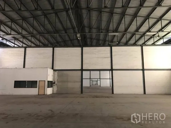 Warehouse for rent in Khlong Luang, Pathum Thani - Open storage bay with steel-framed partition wall and adjoining office room with windows and door.