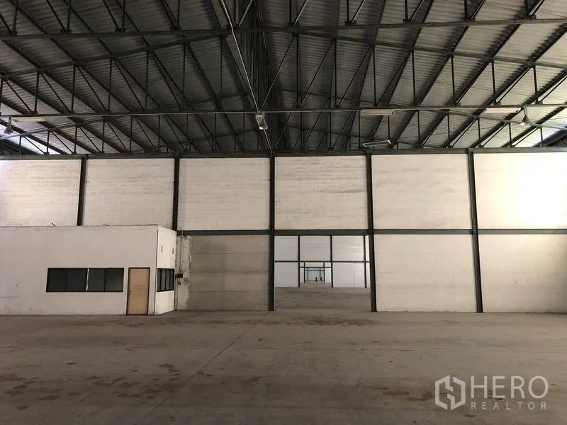 Warehouse for rent in Khlong Luang, Pathum Thani - Open storage bay with steel-framed partition wall and adjoining office room with windows and door.