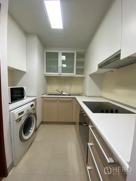 Condominium for rent or sale in Khlong Toei, Bangkok - Galley kitchen with electric cooktop, oven, washing machine and microwave.