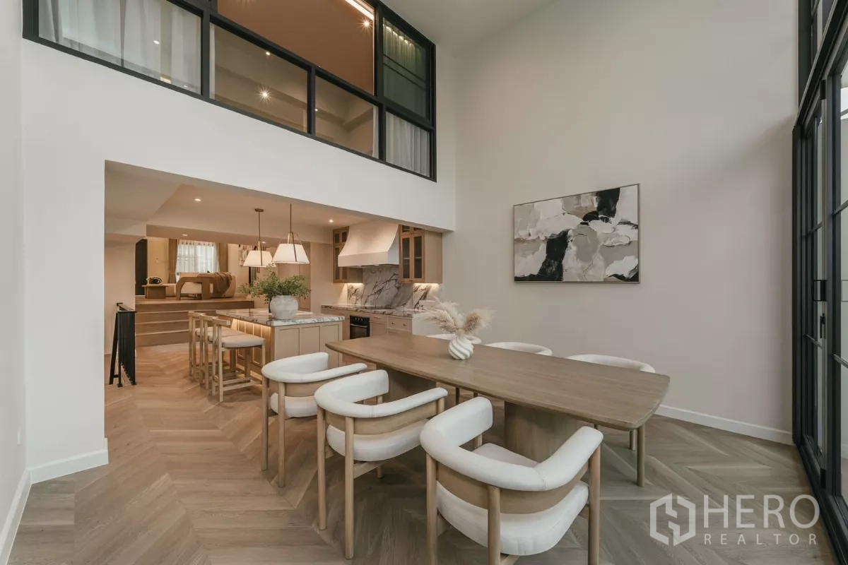 Townhouse for rent in Watthana, Bangkok - Dining area with high ceiling, artwork and mezzanine windows overlooking kitchen.