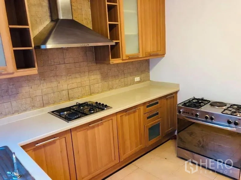 Townhouse for rent in Khlong Toei, Bangkok - Fitted kitchen featuring wooden cabinets, gas hob, range hood and stainless-steel oven.