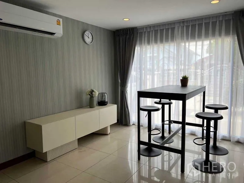 Detached House for sale in Mueang Pathum Thani, Pathum Thani - Dining area with high table and stools beside floor-to-ceiling curtains and AC