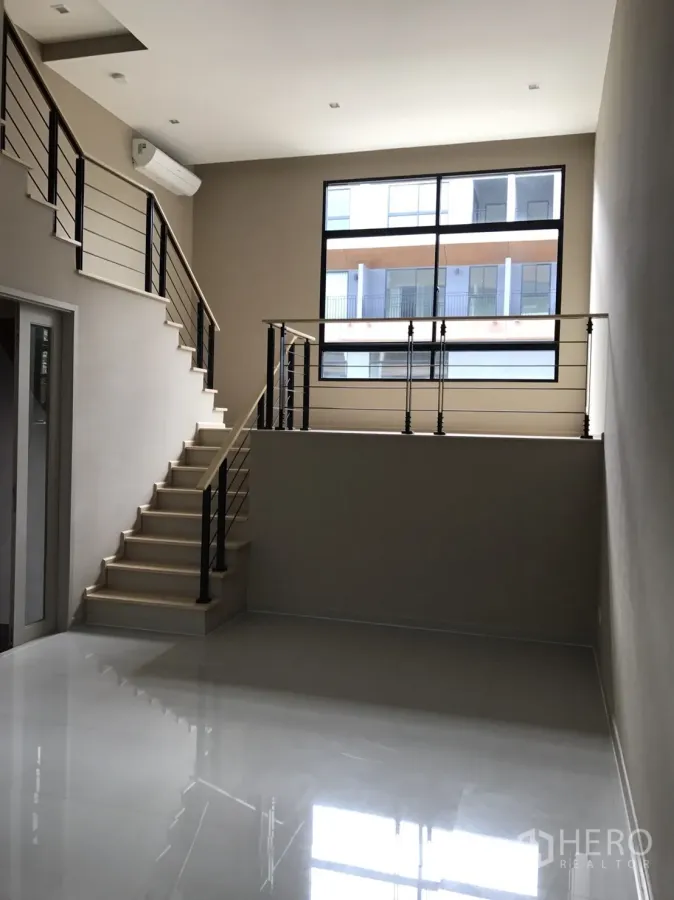 Townhouse for sale in Suan Luang, Bangkok - Double-height living room with glossy tile floor, modern staircase and a large window.