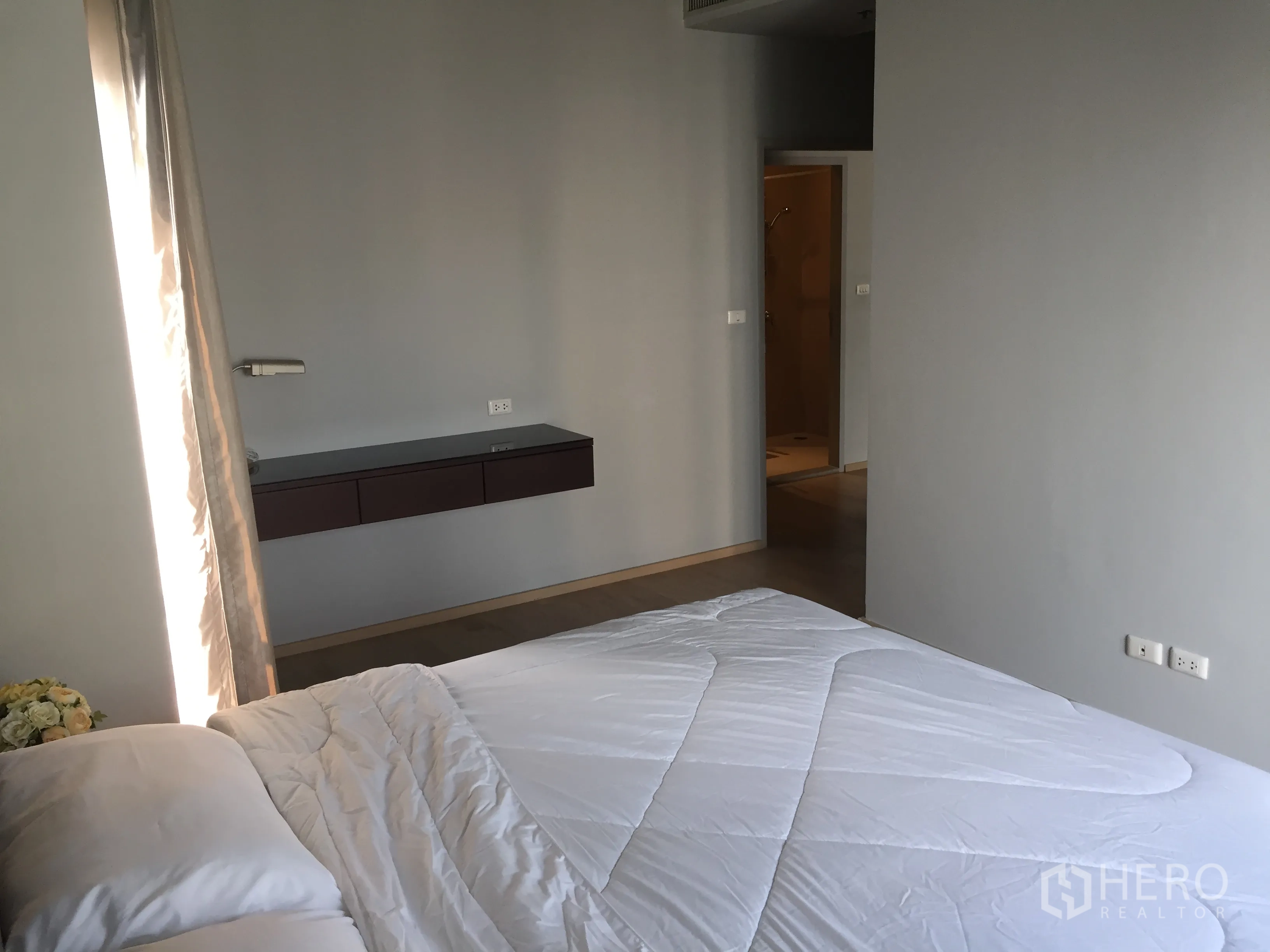 Condominium for rent in Bangkok - Master bedroom with floating console and doorway to an en-suite bathroom.