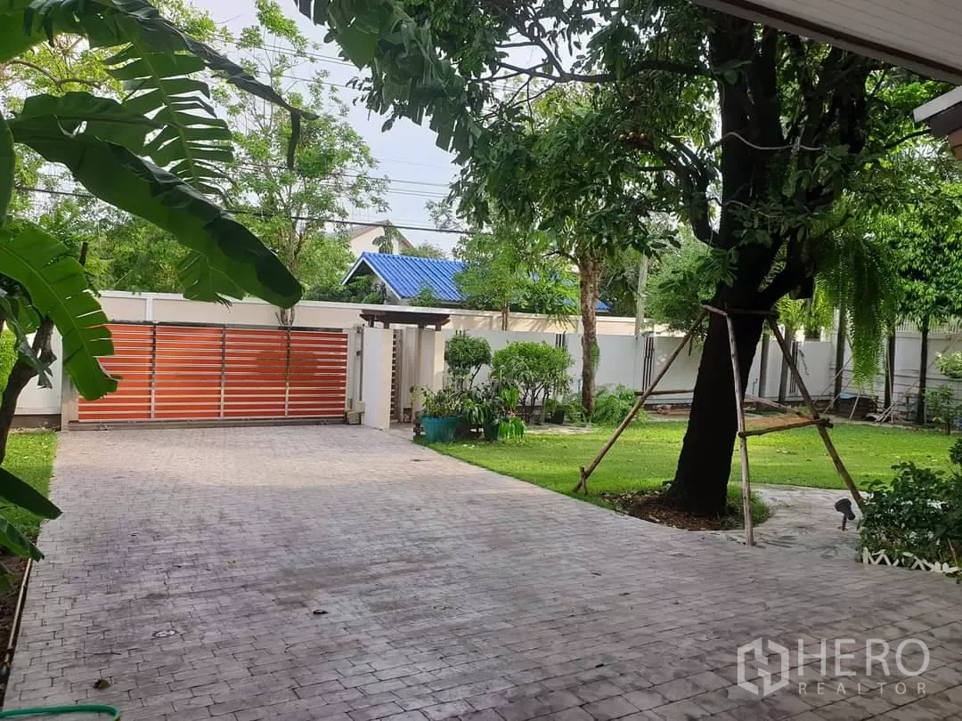 Detached House for rent in Bang Kapi, Bangkok - Wide driveway to sliding gate, surrounded by trees and lawn.