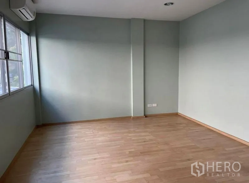 Townhouse for rent in Suan Luang, Bangkok - Large upstairs room with light wood flooring, soft green walls, wide window and wall-mounted air conditioner.