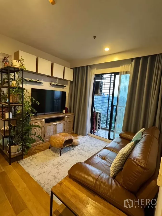 公寓 出租在Watthana, Bangkok - 温馨客厅，皮沙发、电视柜、木地板与通阳台的落地门，城市景观。