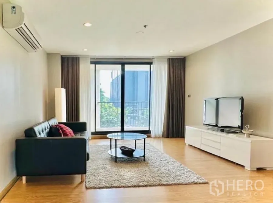 Condominium for rent in Watthana, Bangkok - Spacious living room with sofa, TV unit and sliding doors to the balcony.